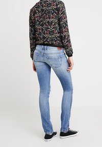 Jean skinny bleu clair avec une texture délavée, doté d'une taille mi-haute et d'un design de poche arrière. Associé à un haut noir à motif floral et des baskets.