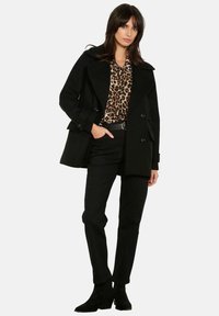 Schwarzer Peacoat mit breiten Revers, doppelreihigen Knöpfen und Seitentaschen über einem Leopardenmuster-Oberteil, kombiniert mit schwarzen Hosen und Stiefeletten.