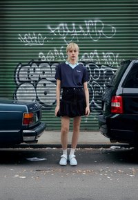 Tumši zils ribots polo ar gaiši zilu apkakli, kopā ar melnu džinsa svārku ar volāniem. Apavi ir baltas zeķes un gaiši zili apavi.