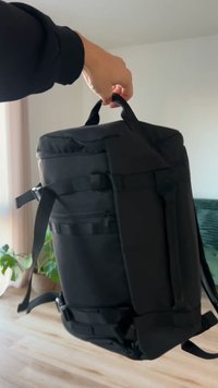Black backpack with a cylindrical shape, durable fabric, side pockets, adjustable straps, and a top handle for easy carrying.