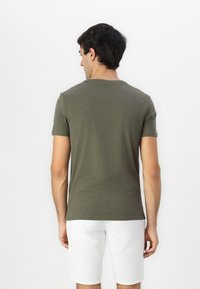 Olivgrünes kurzärmliges T-Shirt aus weichem Stoff, mit Rundhalsausschnitt und lässiger Passform, getragen mit weißen Shorts.