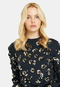 Granatowy sweter zdobiony metalowymi, kwiatowymi cekinami, okrągły dekolt, długie rękawy, miękka tekstura, z równomiernym wzorem na całej tkaninie.