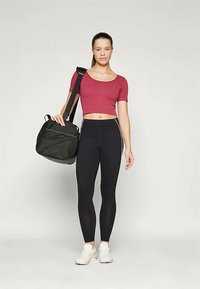 Raudonas trumpas viršus, juodos legginsai ir baltos sportbačiai. Laiko juodą maišą su petnešomis. Lycra medžiaga, prigludusi konstrukcija, minimalus raštas.