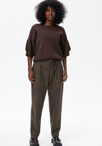 Bruine gebreide trui met een brede halslijn en losse mouwen, gecombineerd met hooggerokte, donkerbruine, gestructureerde broeken met een trekkoord.