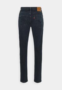 Jean droit bleu foncé vu de dos avec deux poches plaquées et un patch de marque en cuir marron sur la ceinture.