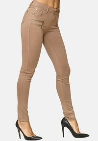 Tunna slim-fit byxor i elastiskt tyg, med två framfickor med dragkedja och en slät yta, i kombination med svarta högklackade skor.