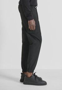 Zwarte cargobroek met een elastische tailleband en boorden, voorzien van zijzakken. Gecombineerd met zwarte gestructureerde sneakers.