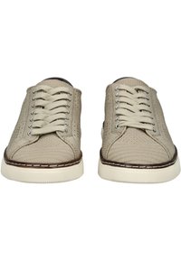 Tenisi beige din pânză cu o suprafață texturată, închidere cu șireturi și o talpă din cauciuc albă. Prezent pe marginea tălpii o cusătură maronie.