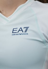 Svijetloplava atletska majica izrađena od glatkog materijala, s V-izrezom i ukrašena mornarsko plavim EA7 Emporio Armani logotipom.