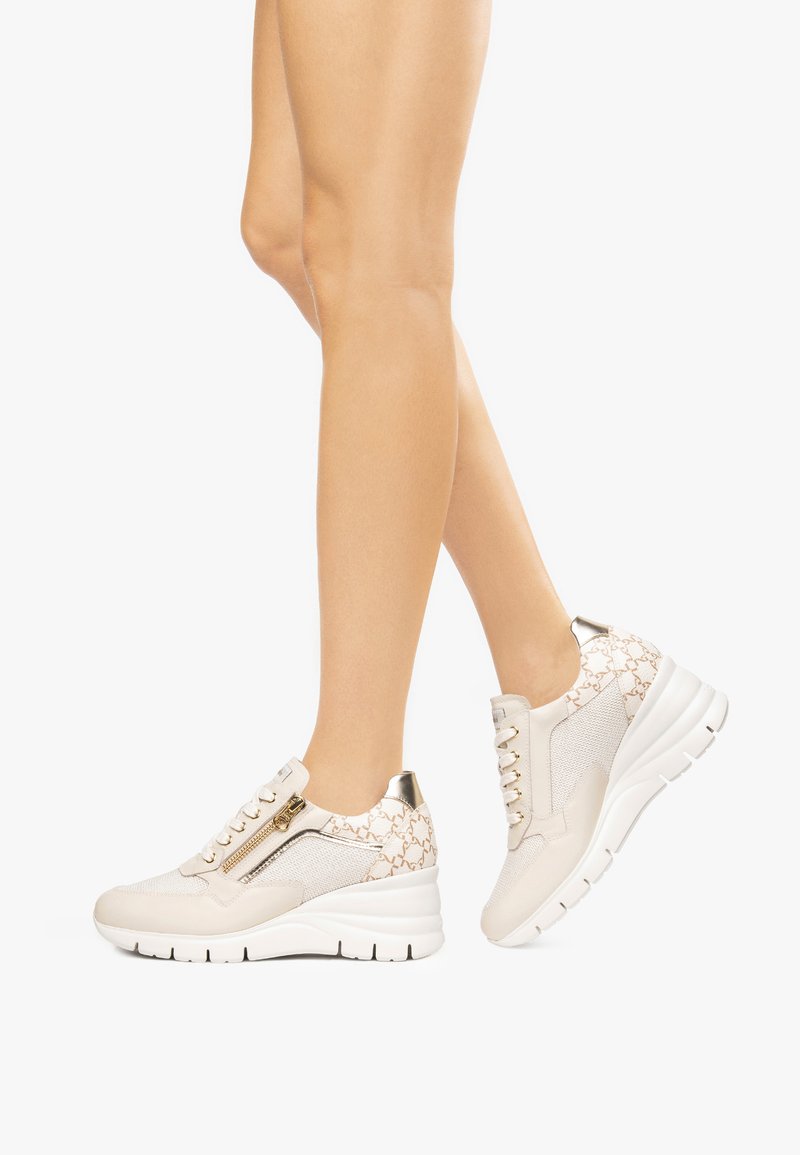Sneakers a zeppa beige con tomaia in tessuto testurizzato, dettagli dorati e chiusura con zip. La suola è bianca con scanalature orizzontali per una migliore aderenza.