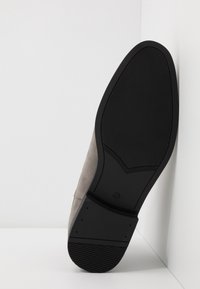Zapato de ante gris con suela de goma negra. La suela presenta una superficie texturizada para mayor agarre, además de un diseño de punta redondeada.