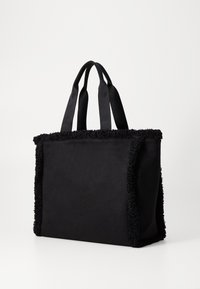Sac fourre-tout noir à surface lisse, doté d'une bordure en peluche texturée. Il possède deux anses en tissu et une forme rectangulaire.