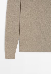 Beżowy sweter dziany z teksturowanym wzorem, długimi rękawami i prążkowanym dołem. Materiał wydaje się miękki i lekki.