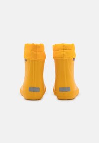 Des bottes imperméables jaunes avec une tige texturée, un revers pliable et une bande réfléchissante à l'arrière pour la visibilité. Semelle en caoutchouc souple.