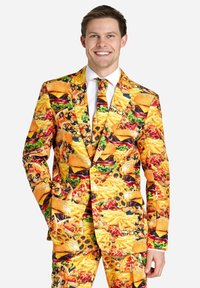 Traje de colores brillantes cubierto de varios estampados de comida, incluyendo hamburguesas, papas fritas y pizza. Presenta una corbata a juego con un diseño similar.