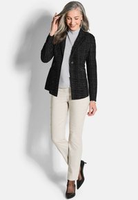 Blazer noir texturé à deux boutons, porté sur un haut gris clair, associé à un pantalon crème et des escarpins noirs pointus, présentant une allure soignée.