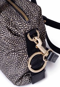 Nahaufnahme einer gemusterten Stofftasche mit einem goldenen Reißverschluss und einem schwarzen Riemen, der mit einem goldenen Haken und Ring befestigt ist.