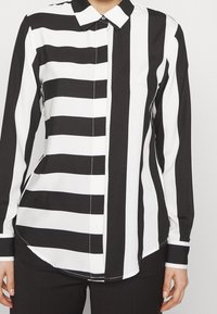 Langärmliges Hemd mit Knöpfen, das abwechselnd dicke schwarze und weiße Streifen zeigt, klassischen Kragen und abgerundetem Saum. Elegante, glatte Stofftextur.