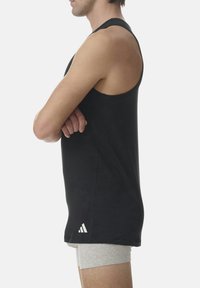 Černý bezrukávový top vyrobený z lehkého materiálu, s minimalistickým designem a bílým logem Adidas blízko spodního lemu.