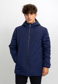 Piumino blu navy con cappuccio, cerniera frontale e tasche laterali. Tessuto liscio con finitura leggermente imbottita. Design minimalista.