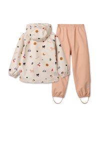 Lahka dežna jakna kremne barve z barvnimi živalskimi in vzorčnimi motivi, kombinirana s breskvasto obarvanimi nepremočljivimi hlačami.