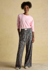 Svetloružová košeľa s dlhým rukávom v kombinácii s voľnými čiernymi nohavicami s farebným kvetinovým vzorom a elastickým pásom. Viditeľná jemná textúra.