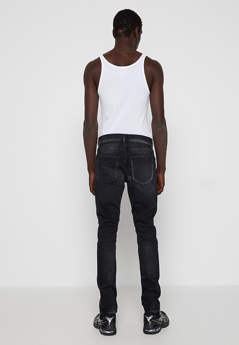 Schwarze Slim-Fit-Jeans mit mittelhohem Bund, zwei Gesäßtaschen und einer glatten Textur, kombiniert mit einem weißen Trägershirt.