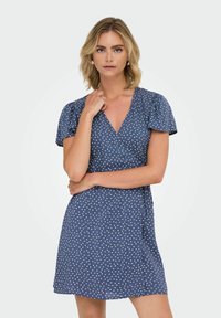 Mörkblå omlotklänning med små vita hjärtformade mönster, korta puffärmar och v-ringning. Lättviktig tyg, knälång design.