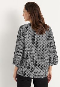 Schwarz-weiße gemusterte Bluse mit Dreiviertelärmeln, die ein geometrisches Design und eine lockere Passform aufweist, aus leichtem Material gefertigt.