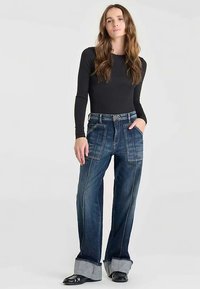 Jeans de corte ancho hechos de denim azul oscuro, con bolsillos de parche, costuras contrastantes y dobladillos remangados con una textura de denim más clara.