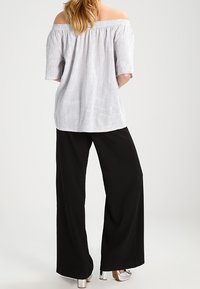 Off-Shoulder gestreifte Bluse in Weiß und Marineblau, mit lockerem Schnitt und kurzen Ärmeln; kombiniert mit weiten schwarzen Hosen und silbernen Heels.