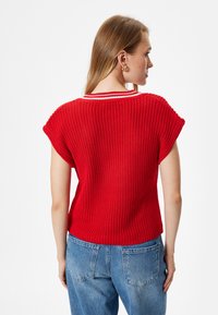 Top de punto rojo con mangas cortas, que presenta un cuello de rayas blancas. La textura es de canalé, diseñado con un corte holgado y un dobladillo redondeado.