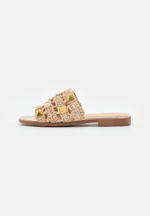 Flad beige vævet slide-sandal med gyldne pyramidestuds og hvide perleaccenter på bred rem, brun sål.