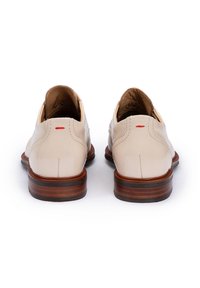 Scarpe in pelle beige con una texture liscia, dotate di una suola in legno marrone e un piccolo accento rosso sul tallone. Vista posteriore mostrata.