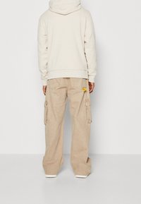 Beige cargobroek met wijde pijpen, zijzakken en achterzakken. De stof heeft een zachte textuur en past goed bij een licht beige hoodie.