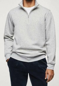 Sweat-shirt gris clair à fermeture éclair, fabriqué en tissu doux, avec un col montant, des poignets côtelés et un ourlet ajusté, associé à un pantalon en velours côtelé bleu marine.