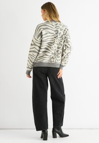 Woman with shoulder-length blonde hair wears a gray and white animal print sweater, black wide-leg jeans, and black heeled ankle boots, standing.