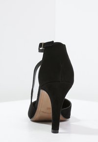 Černá semišová vysoká podpatková bota s kotníkovým páskem, elegantní design, tvarovaný tvar a špičatá špička. Výška podpatku přibližně 10 cm.