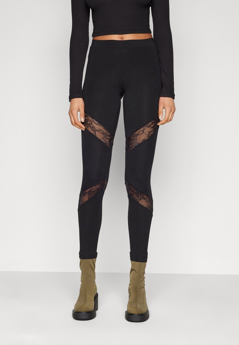 Zwarte leggings met kanten accenten in een zigzagpatroon op de dijen, gecombineerd met olijfgroene enkellaarsjes. Glad stoffen afwerking.