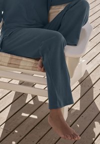 Wygodny niebieski komplet odzieży do wypoczynku z luźną bluzą i spodniami, leżący na jasnym drewnianym tarasie, odsłaniający bose stopy.