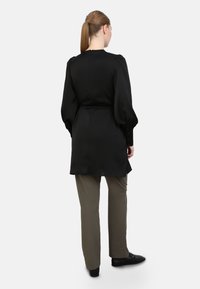 Black long-sleeve shirt dress with a cinched waist, features puff sleeves and button accents, paired with straight olive pants and black shoes.