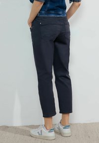 Mörkblå cropped jeans med en klassisk passform, med bakfickor och en slät, matt yta. Bärs med vita sneakers.