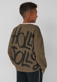 Oliwkowa bluza z okrągłym dekoltem i luźnym krojem, z czarnym grafikiem w stylu sprayu z napisem "HOLD DOLLS" na plecach.