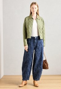 Tikkidega oliiviroheline jakk, millel on krae, valge särk, laiad sinised mustriga teksad ja beežid sääre kõrgused saapad. Käes kantakse pruuni käekotti.