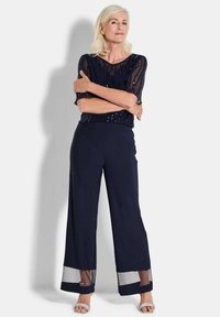 Marine-brede broek met doorschijnende mesh manchetten. De top heeft een doorschijnend, textuurontwerp met pailletten, waardoor een gelaagd effect ontstaat.