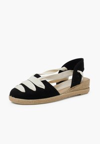Espadrilky s černým tkaným svrškem a bílými pásky, otevřeným zadním dílem a vlněnou podrážkou.