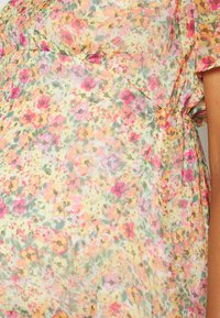 Vestido de maternidade floral em tecido leve, com uma mistura de cores rosa, amarelo e verde, apresentando franzidos na lateral para ajustabilidade.