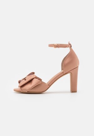 Sandale à talons hauts rose blush avec bride cheville et grand nœud décoratif sur la bride avant, vue de côté sur fond blanc.