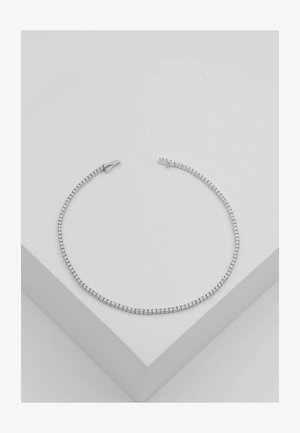 Silbernes Tennisarmband mit kleinen runden klaren Steinen in einer einzelnen Reihe, liegend auf einer weißen geometrischen Oberfläche.