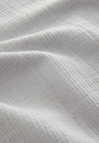 Tejido texturizado en un suave tono gris claro con sutiles rayas horizontales y verticales, que presenta un aspecto suave y tejido, con un acabado ligeramente arrugado.